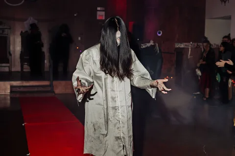 A woman dressed as a long-haired horror ghost reaches her hands out on the runway.