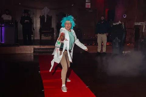 The mad scientist costumed woman walks the runway with hair blown by motion.