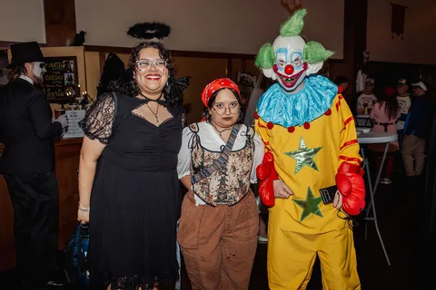 A woman in black, a man in a vest and a colorful clown pose together.