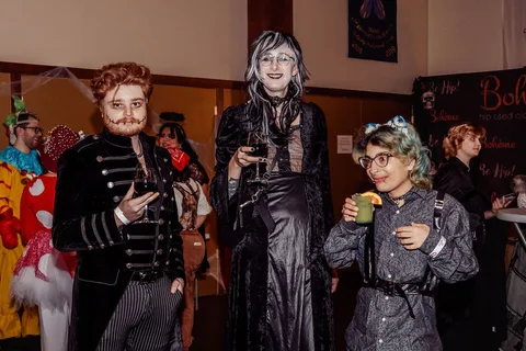 A group of guests in costume, including a clown at the edge of frame, stand together.