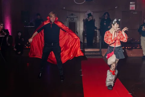 A man in a black cape leaps mid-motion on the red carpet runway.