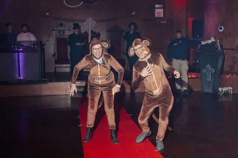 Two guests in monkey costumes walk mid-stride on the red carpet runway.