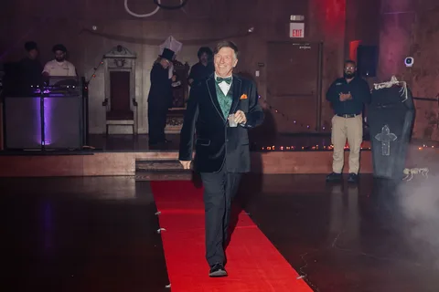 A man in a black tuxedo walks alone, seen at a distance on the runway.
