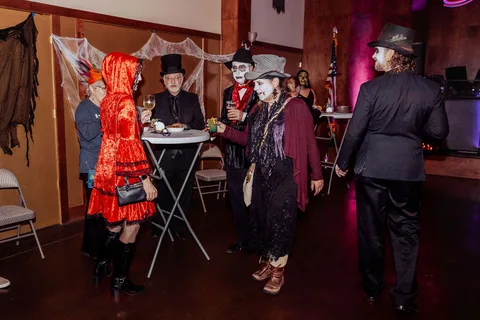 Guests in costume stand and talk on the dance floor under dim lighting.