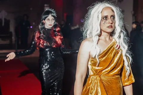 Two women in black sequin and gold gowns walk the runway together.