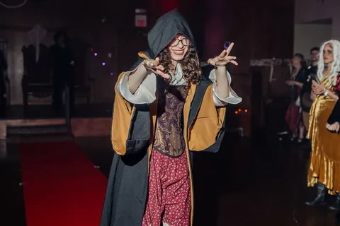 A woman in a hooded costume gestures playfully at the camera.