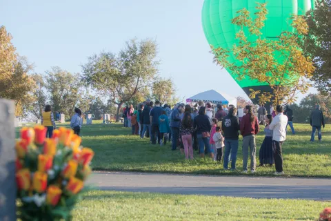 A long line of people crosses the grass field as the balloon floats in the distance.
