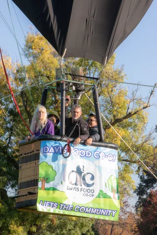 Two balloon riders look over the basket beside the Davis Food Co-op banner.