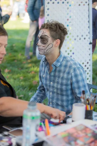 A teen in a plaid shirt shows off skull face paint in profile against a white lattice backdrop.