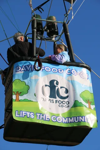 A close view of a hot air balloon basket banner reading Davis Food Co-op Lifts the Community.