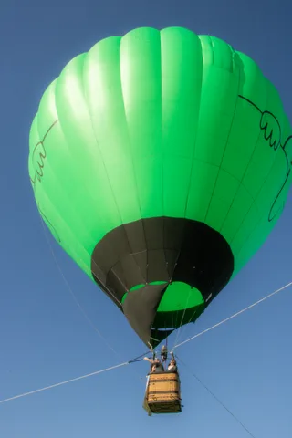 The green balloon envelope rises alone against clear blue sky.