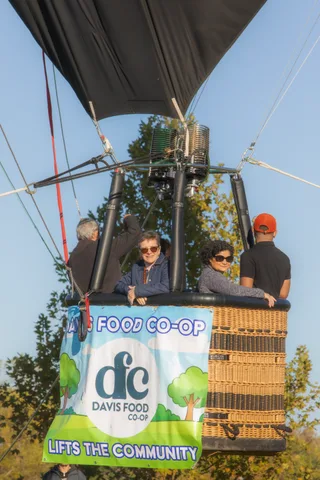 Four riders smile together in the basket under the full Davis Food Co-op logo.