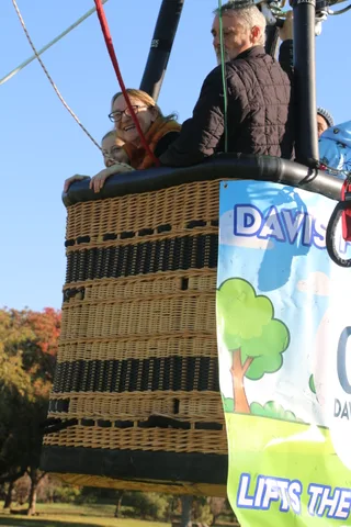 A mother lifts her child up to see over the basket rim as a grandfather looks on.
