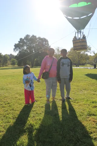 The balloon and basket appear washed out by strong sun flare against the trees.