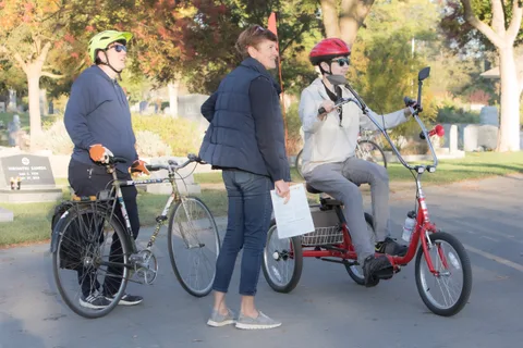 Two riders on adaptive trikes pause together on the street.
