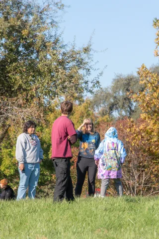 A small group in patterned jackets stands near colorful autumn trees.