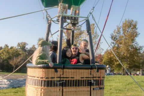Riders throw their arms up in excitement as the basket passes over the event tents.