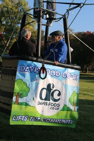 The co-op banner is visible on the basket as the balloon rises past the trees.