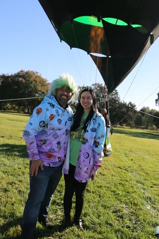 A man in a green wig costume and a woman pose together on the open grass.