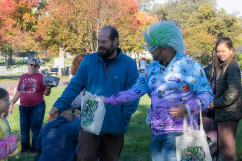 A man in a maroon shirt talks with a costumed volunteer handing out gift bags.