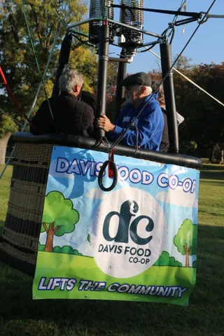 A rider stands in the basket beside the co-op banner as the balloon holds steady.