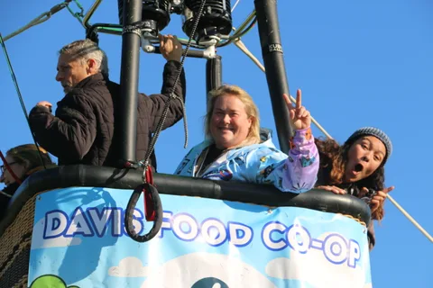 A small group cheers and flashes peace signs from inside a hot air balloon basket.