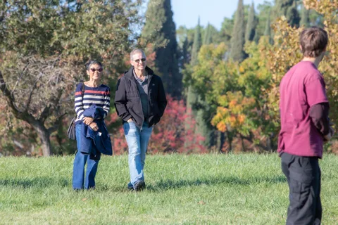 Two onlookers stand on the grass with a man in pink walking past behind them.