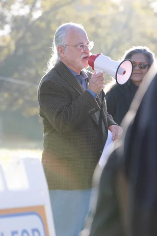 A man speaks into a red megaphone beside a woman in the sunlit field.