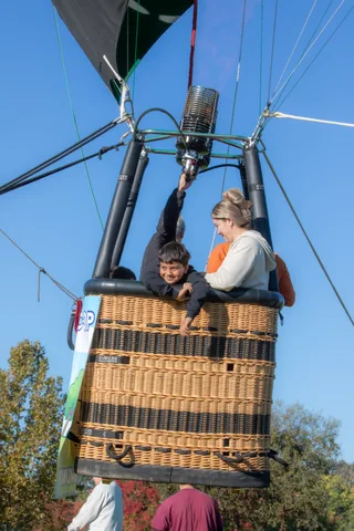 A boy leans out of the basket smiling next to a man in an orange jacket.