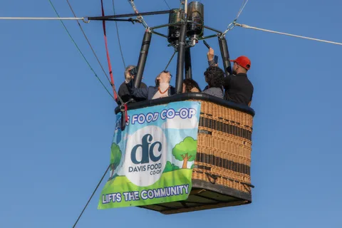 Two riders in caps look out from the basket above the Davis Food Co-op banner.