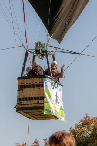 A rider waves from a hot air balloon basket against a clear blue morning sky.