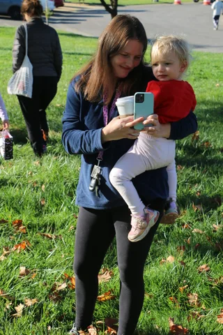 A woman holds a toddler in a red hat while checking her phone.