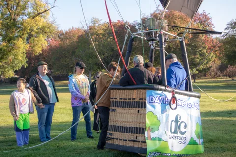 The balloon descends near a cluster of onlookers in the field.