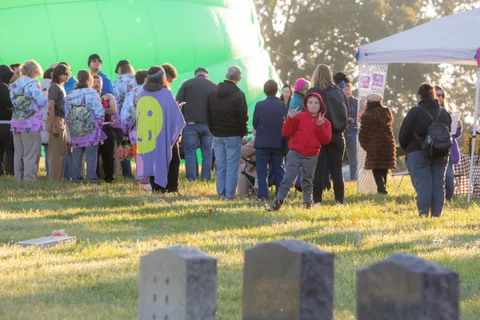 A large crowd gathers near the white tents and photo booth backdrop, backlit by the morning sun.