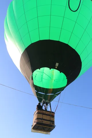 The green balloon envelope fills the sky above its small basket far below.