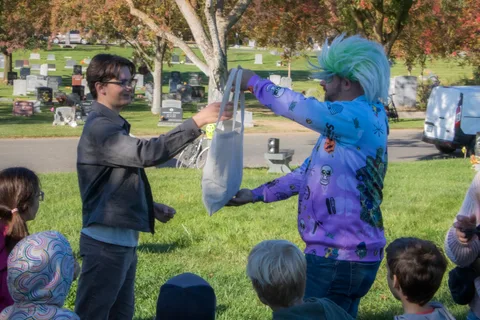 A costumed volunteer with teal hair hands out a gift bag to a guest.