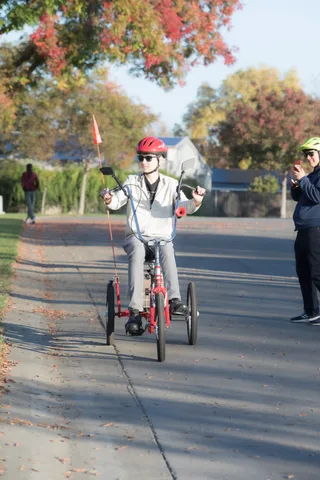 A rider in a full gray costume pedals down a residential street.