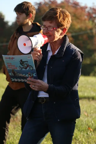 A teenager and an older woman with a megaphone stand together listening to the announcements.