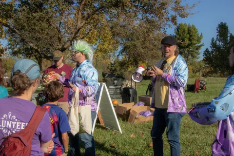 A volunteer speaks through a megaphone next to a sign board with other volunteers nearby.