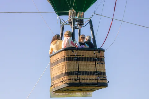 Riders are silhouetted against bright backlit sky in the basket.