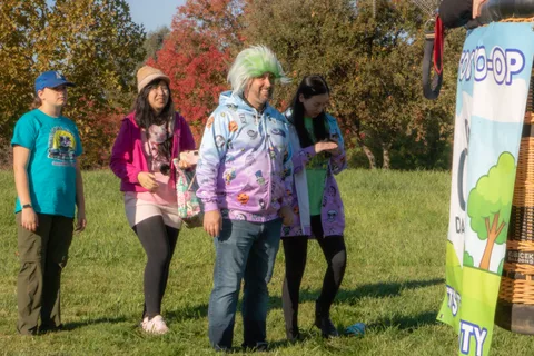 Three guests including a man in a green wig stand near the landed balloon basket.