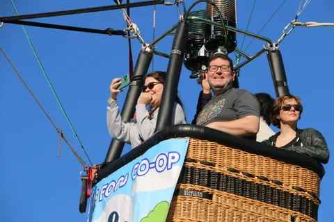 Riders wave and take photos in the basket with the co-op banner below them.