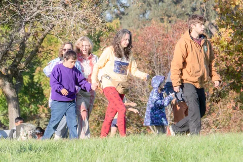 A small group including a boy in purple walks across the grass among the trees.