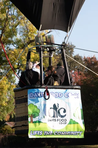 Balloon riders pose above the Davis Food Co-op banner during the tethered ride.