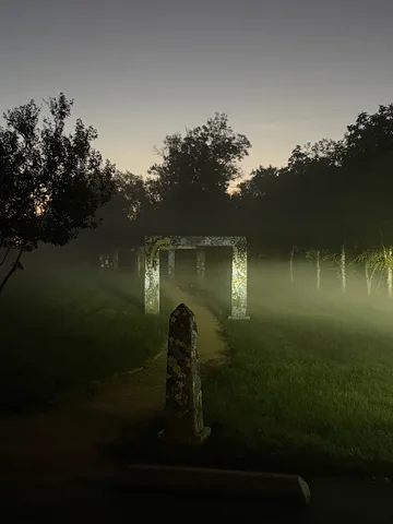 Dark silhouettes of trees and a faint archway before sunrise.