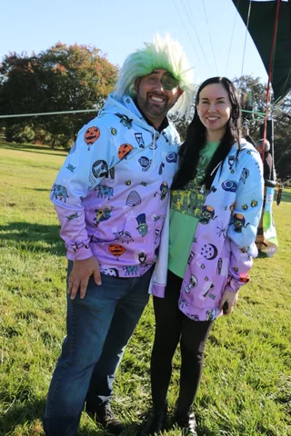A man in a green wig costume poses with a smiling woman on the grass.
