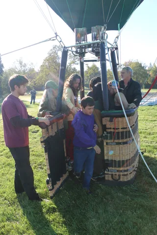 A family gathers on the grass near the balloon crew.