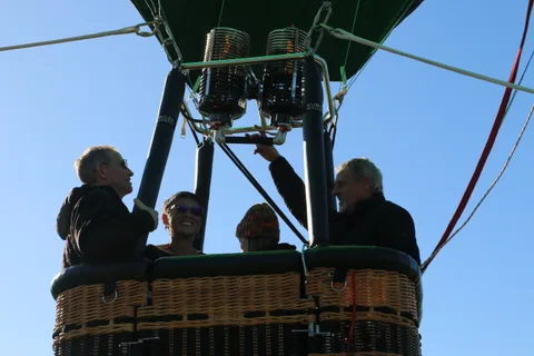 Several people gather around a hot air balloon basket as the burner fires above them.