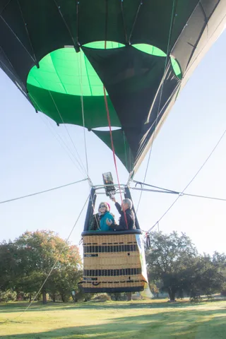 The balloon's canopy fills the sky above its basket and two small riders.