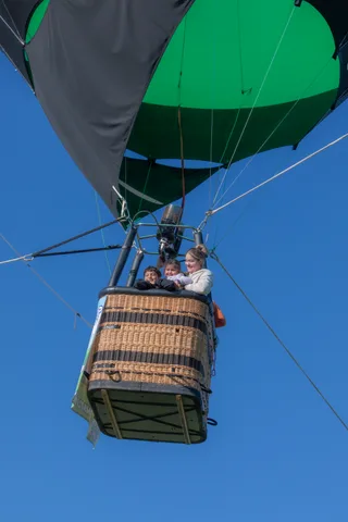The balloon and its basket hang against open sky with rigging lines fanning out above.